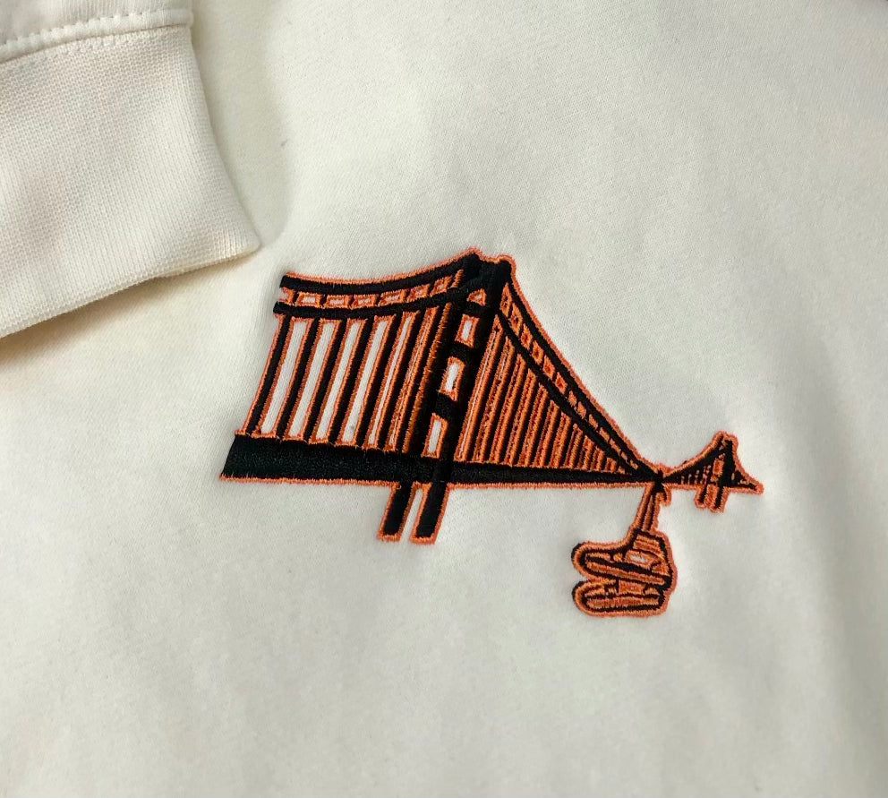 cream colored sf giants themed hoodie with shoes or sneakers hanging from golden gate bridge